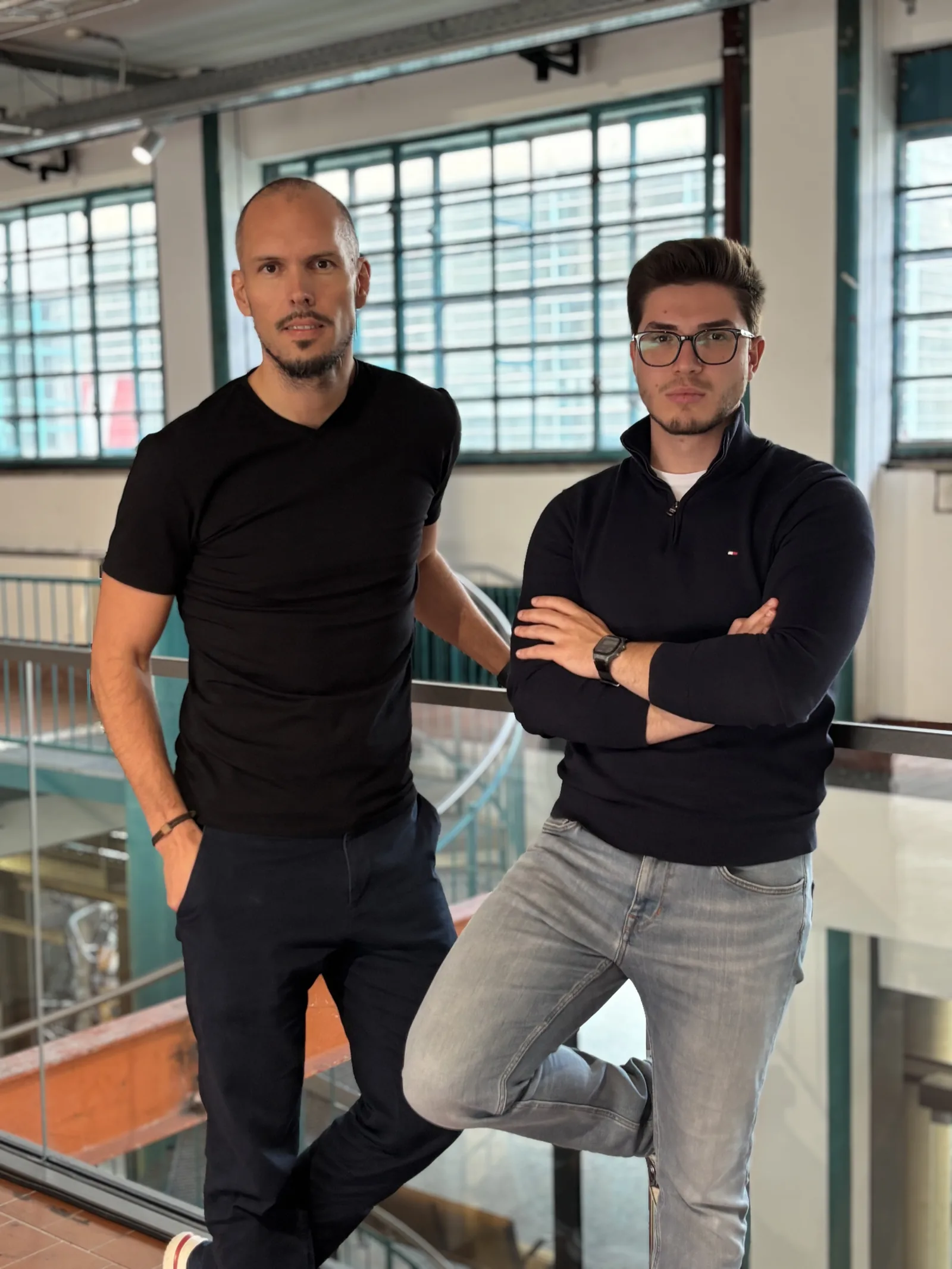 The ALLO-X co-founders Stefan Rotter and Metin Hasan standing at a railing in a bright industrial building.